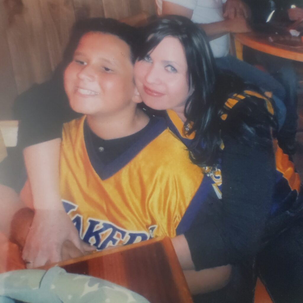 A boy of 9 or 10 is hugged by his mom who is smiling into the camera. 
