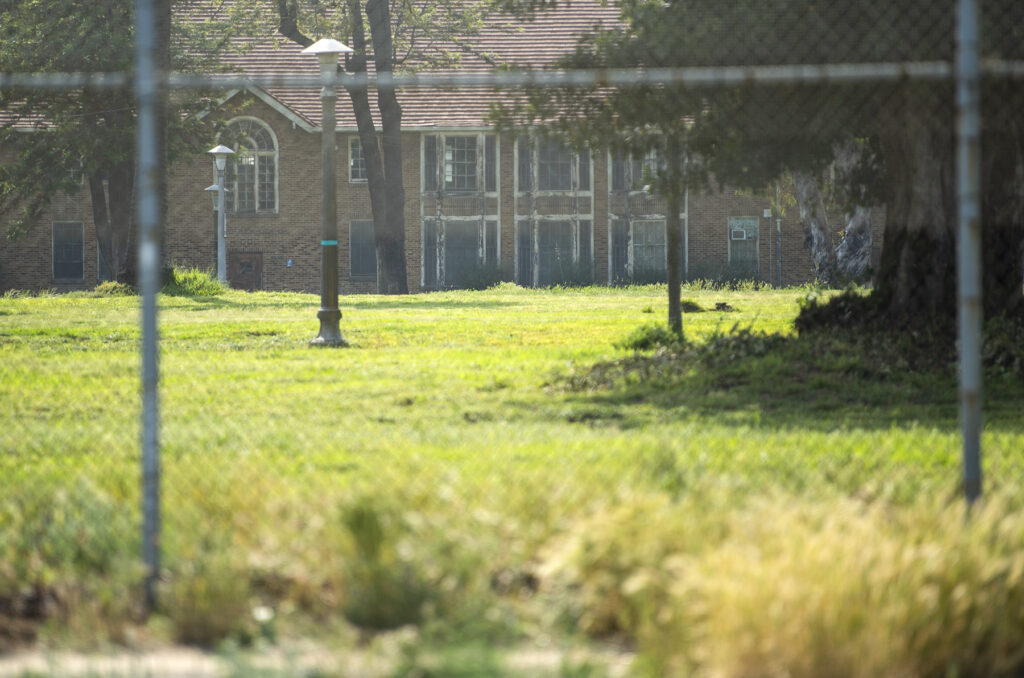 A building in the distance, surrounded by a wire fence and grass. 