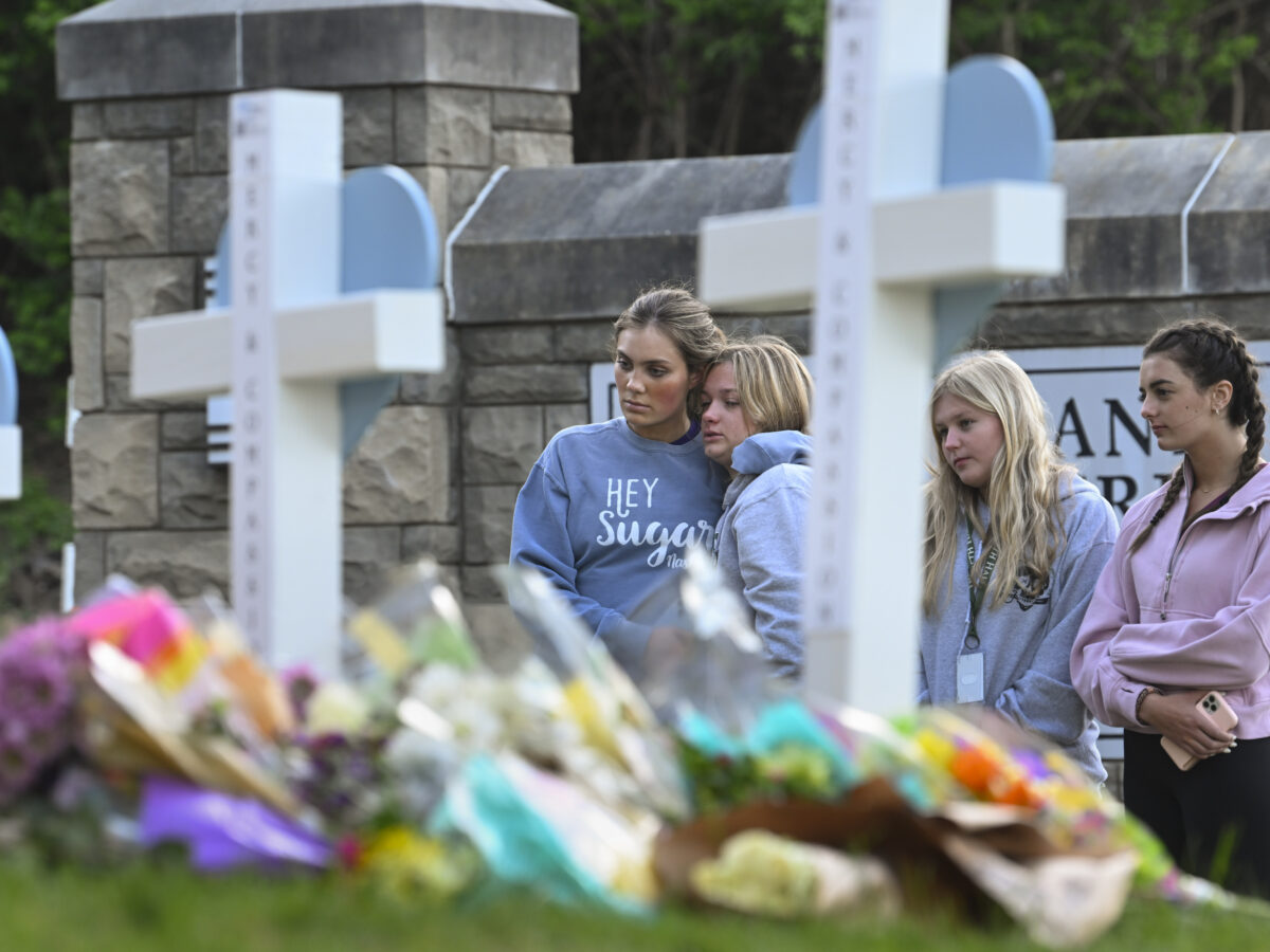 Three girls look at a line of white crosses with flowers at their base.