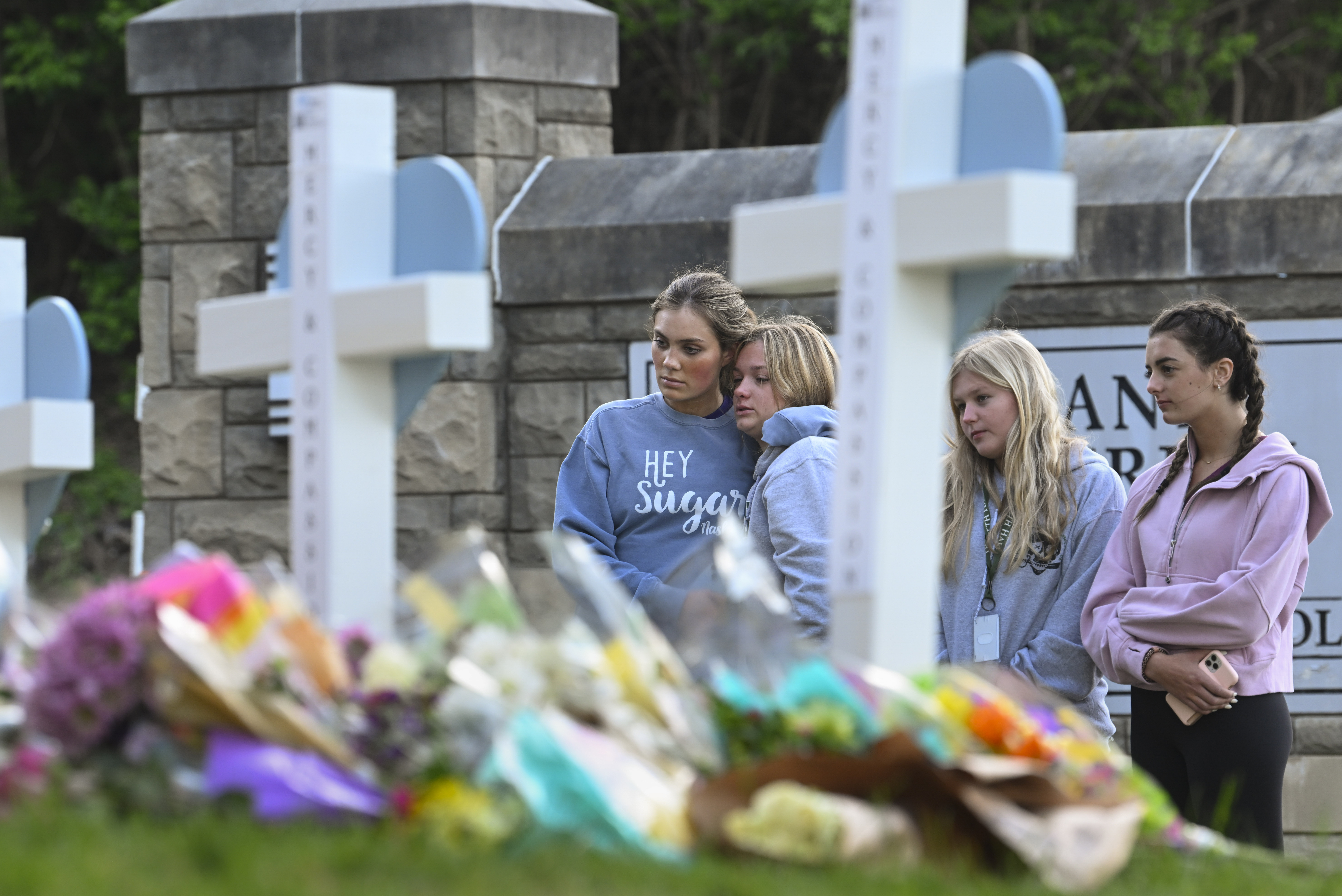 Three girls look at a line of white crosses with flowers at their base.