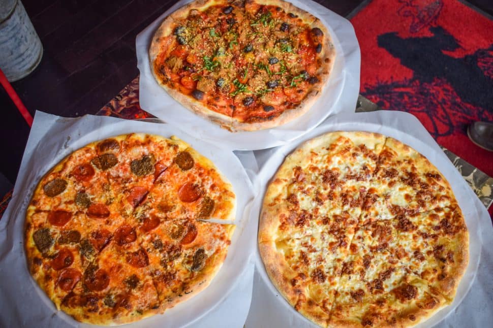 An assortment of pizzas from the 4th Horseman in Downtown Long Beach: The Frailty (vegan pizza) at the top; Angel of Death (blue cheese, bacon, caramelized onion) on the right; and Death to Piggy (Italian sausage, meatball, pepperoni, and bacon) on the left. Photo by Brian Addison.